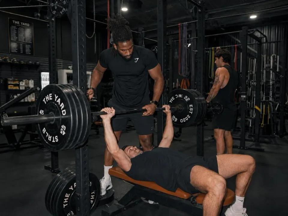 Entrenador asistiendo a un atleta en press de banca